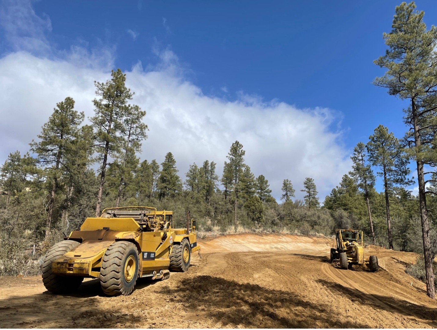 Two bulldozers creating a fire-wise dirt road in the forest.