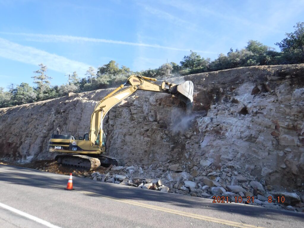 An excavator is working on the side of a cliff along SR 87 Pine Creek Canyon Drive.