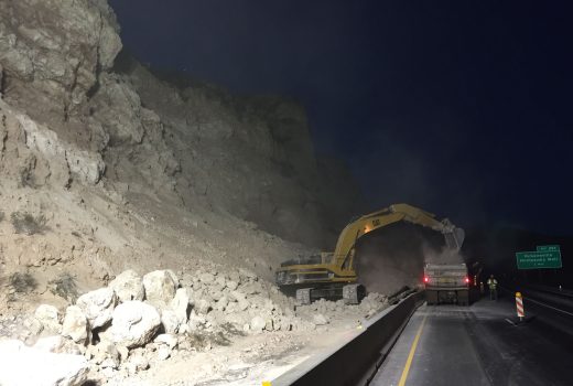An excavator is working on the side of a cliff at night.