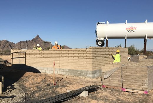 A group of workers are building a brick wall near the Yuma-Casa Grande Highway (I-8) in the desert.