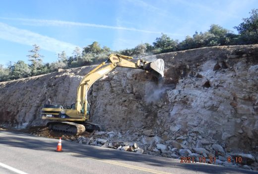 An excavator is working on the side of a cliff along SR 87 Pine Creek Canyon Drive.